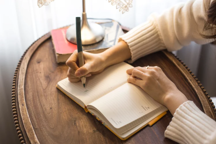 Woman writing on notebook or diary with brown desk