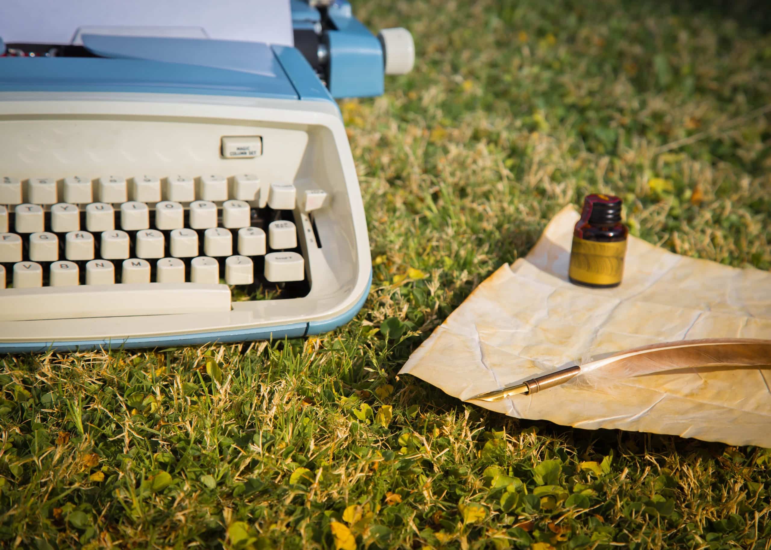 Vintage typewriter sitting outside in the garden with quill, ink bottle, and parchment paper next to it