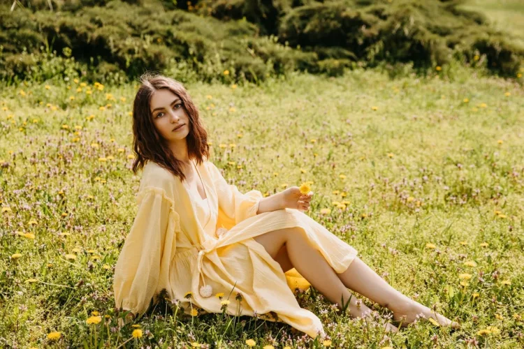 Young barefoot woman wearing a yellow muslin dress, sitting in a field of dandelions