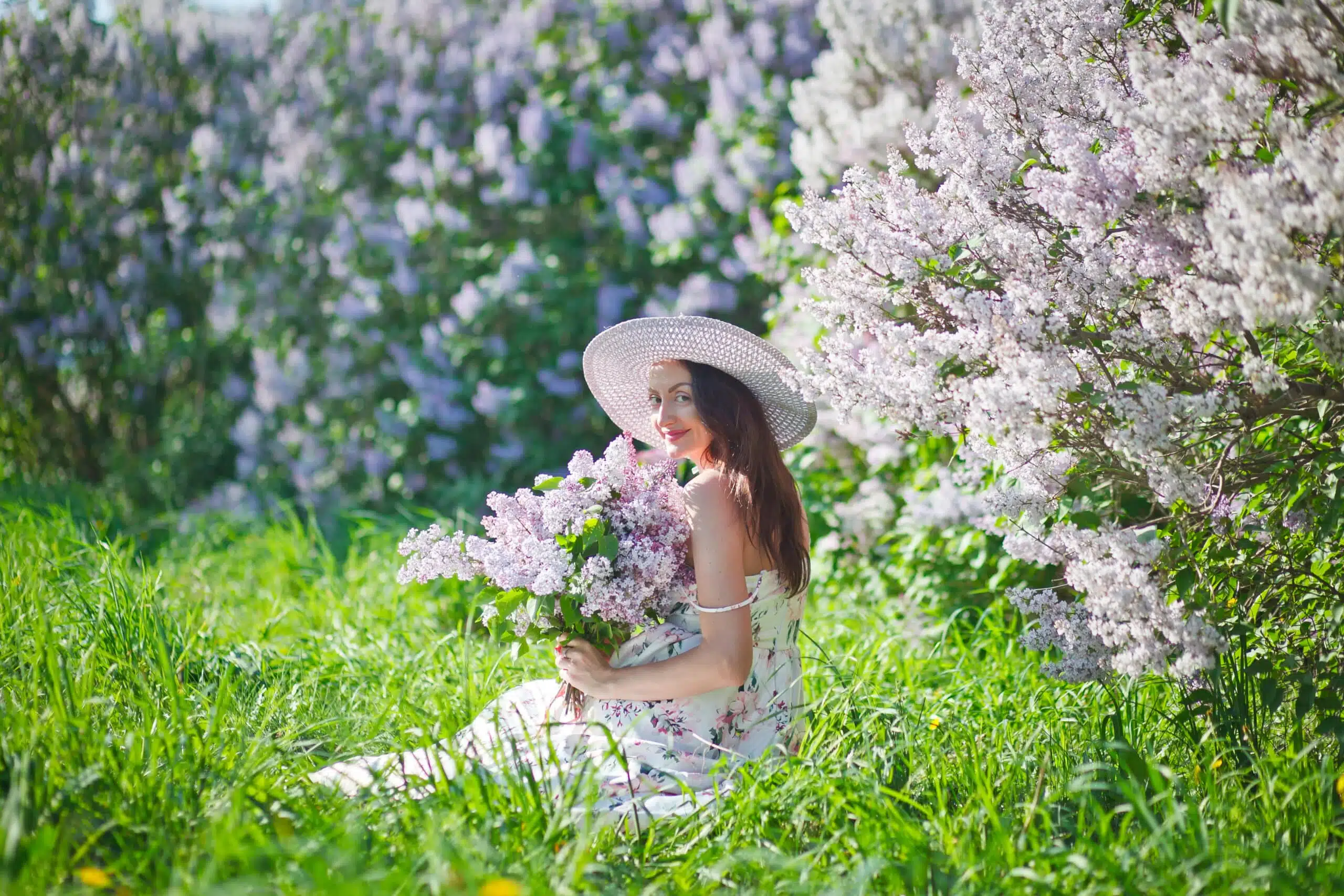 beautiful girl in a hat and in a long dress walks in the garden with a bouquet of lilacs