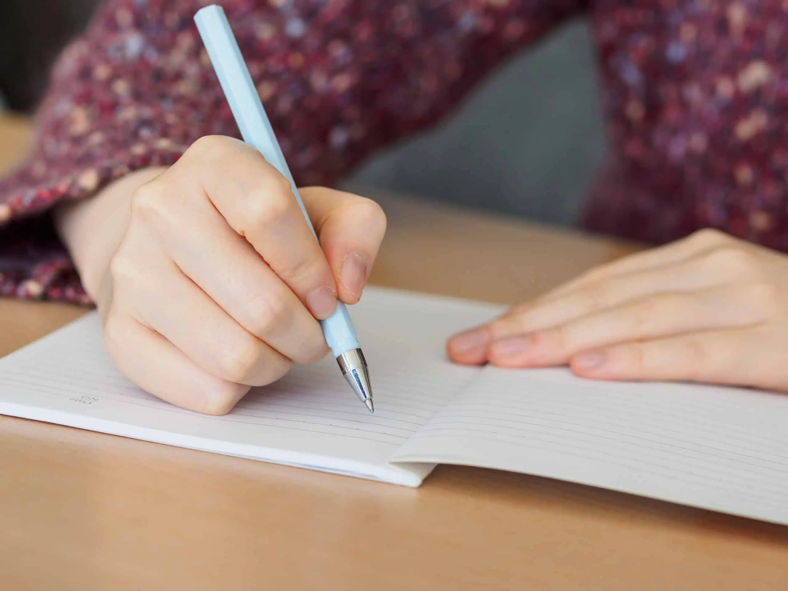 Woman's hands writing in notepad on wooden desk.