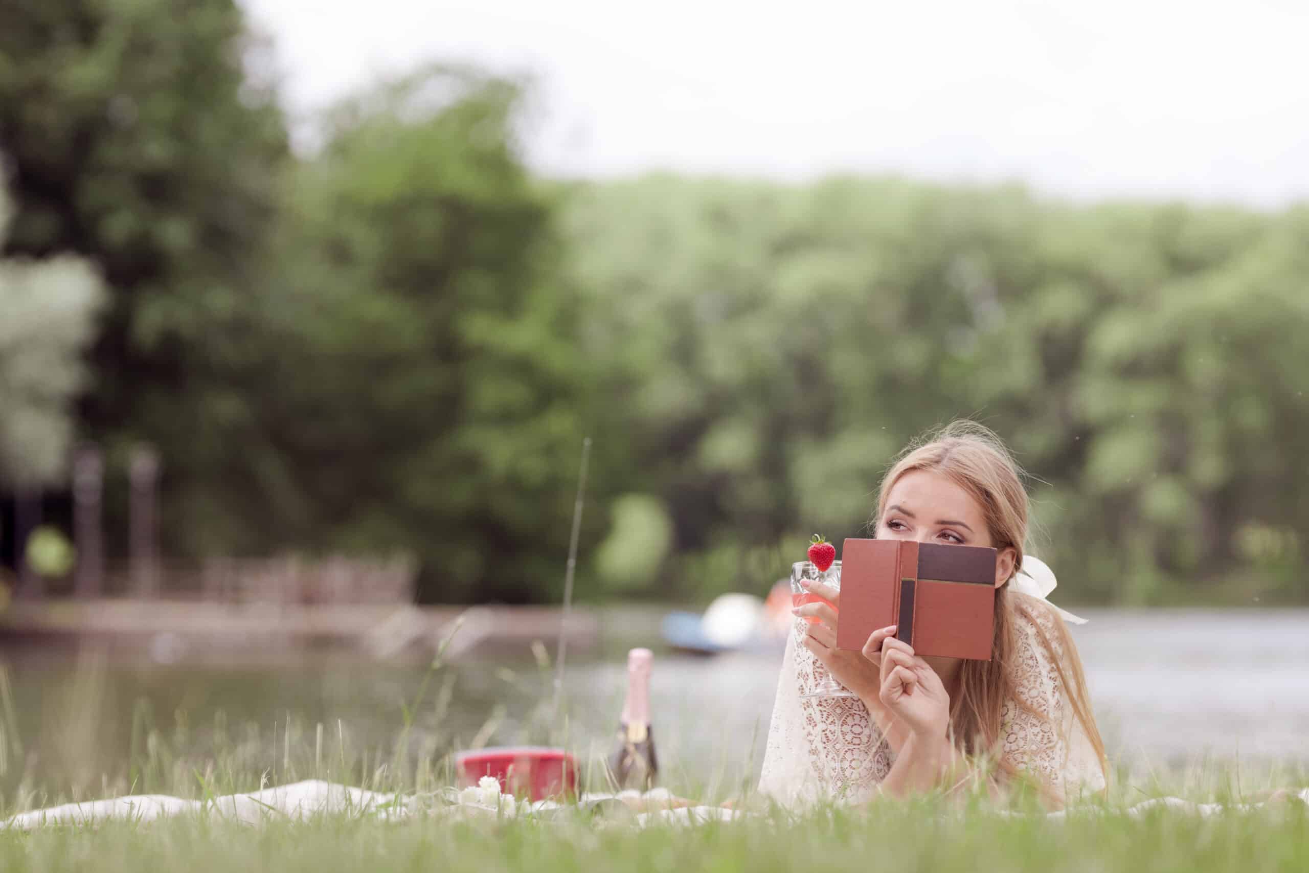 A young lady in a white dress reads a book on the grass.