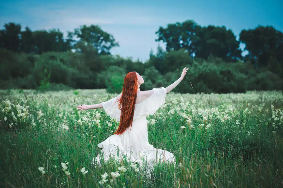 a red-haired enigmatic woman in a white dress on a green field in summer