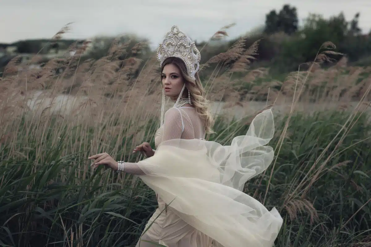 a mysterious lady in white dress and crown running in a field of tall plants