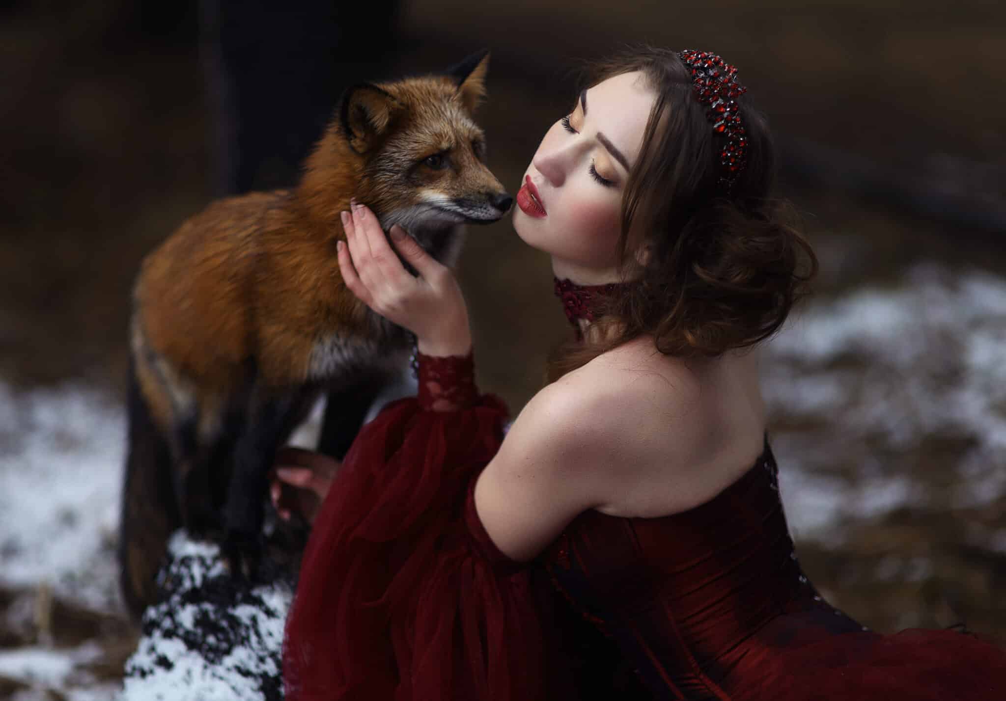 Beautiful young woman in red dress with red fox in forest