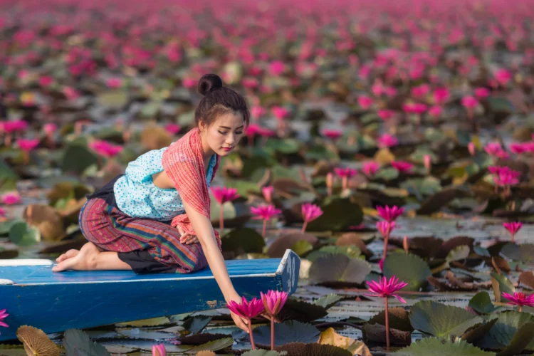 Beautiful Thai lady in Thai dress is holding lotus in the river.