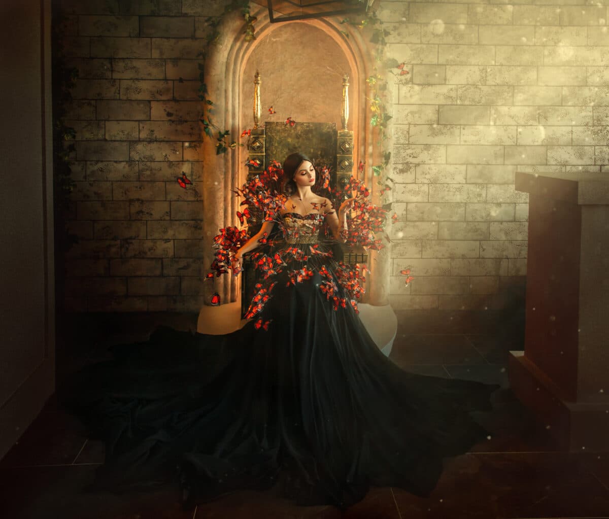 gothic dark queen sits in castle on golden throne. black dress with butterflies. Brick wall, large gothic room, magical sun rays from window. Long train fashionable silk skirt. Glamorous fantasy woman