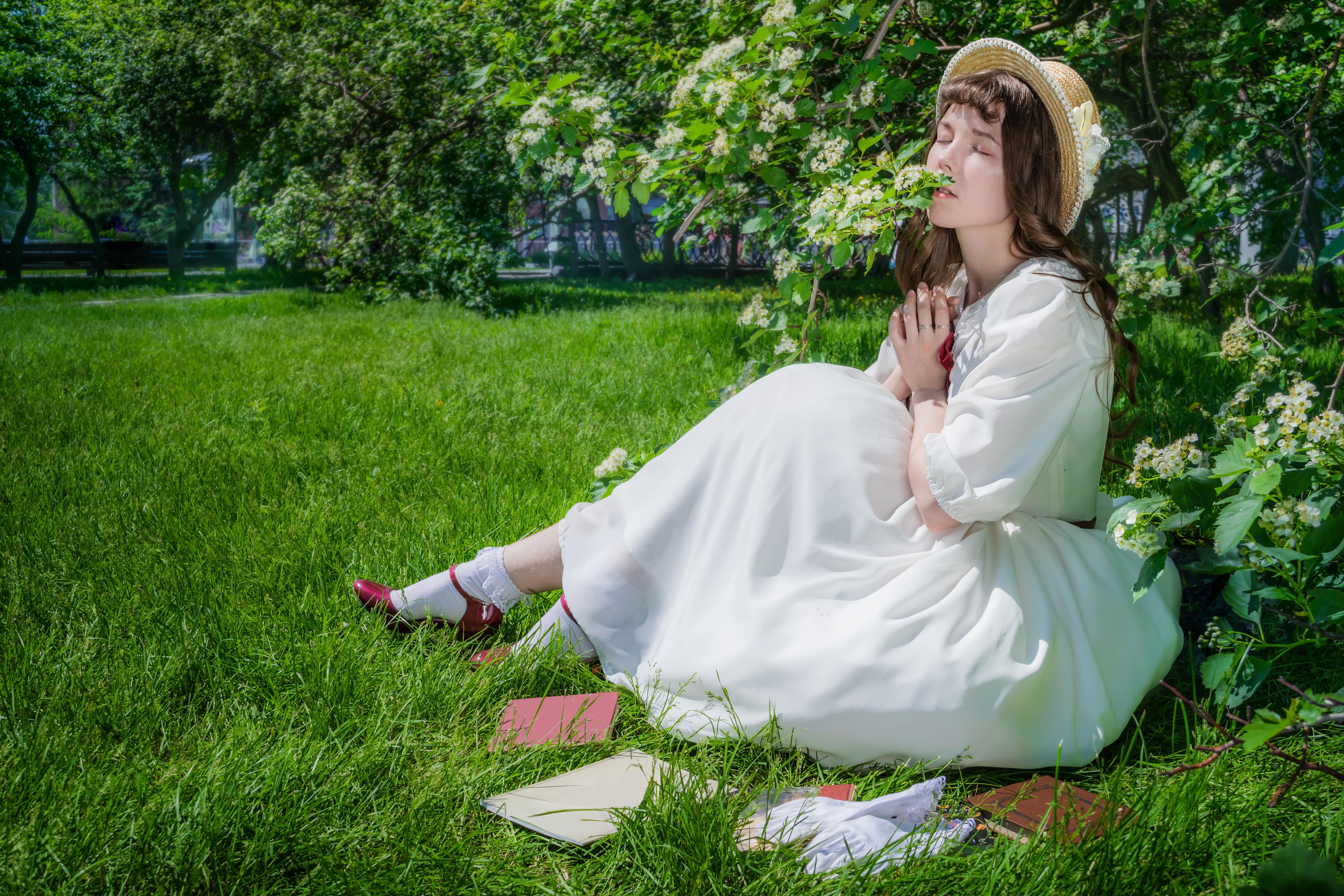 Nice girl in a white dress sits on a lawn in a park