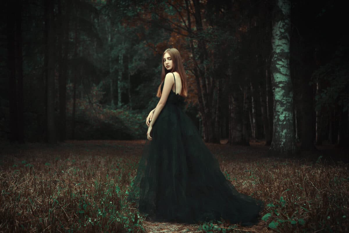 Young girl is posing wearing black dress in a dark forest