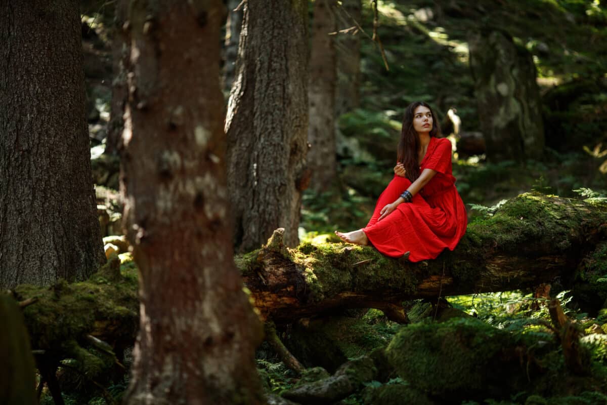 romantic woman in fairy forest relaxing on a tree trunk