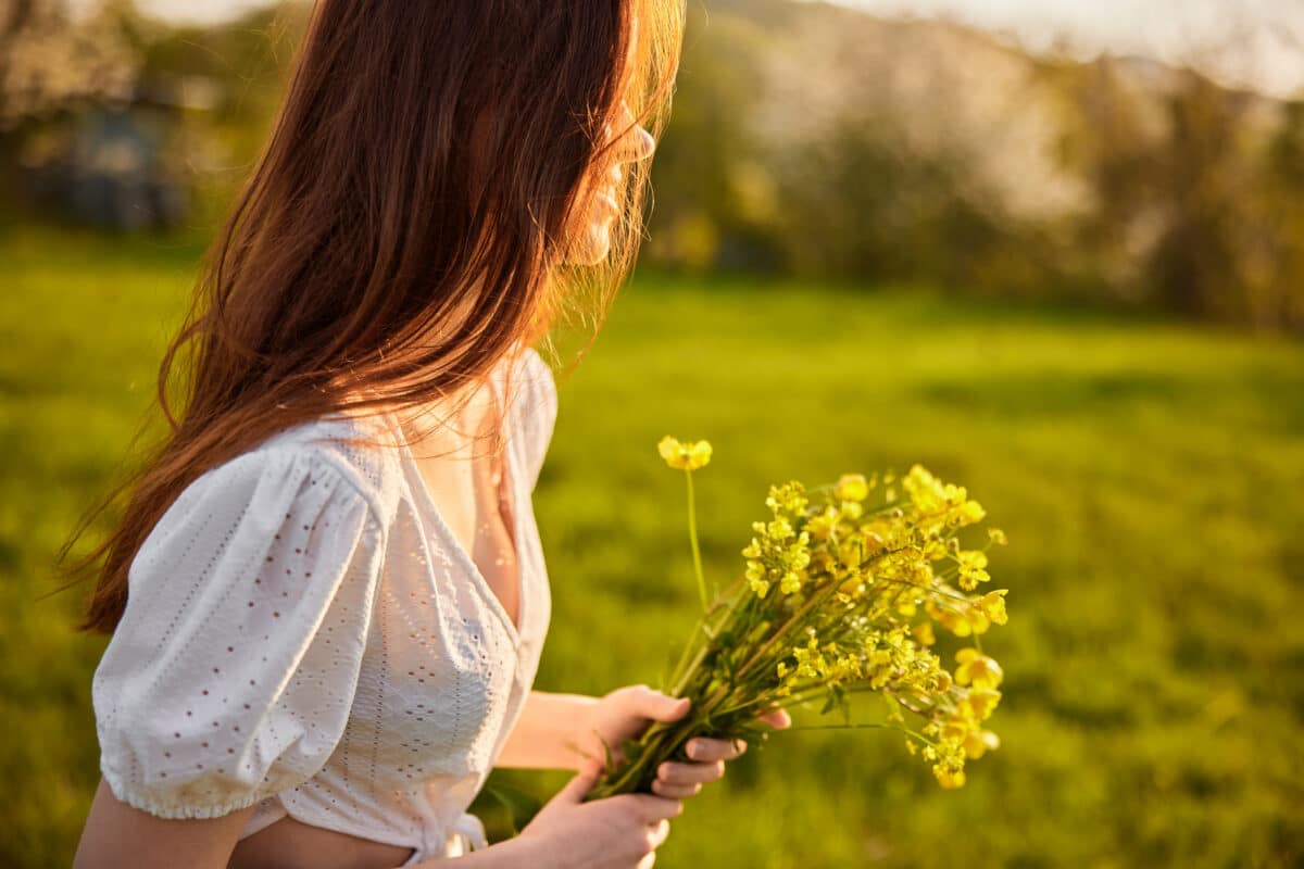 a woman with a bouquet of golden wild flowers in the rays of the setting sun in a field