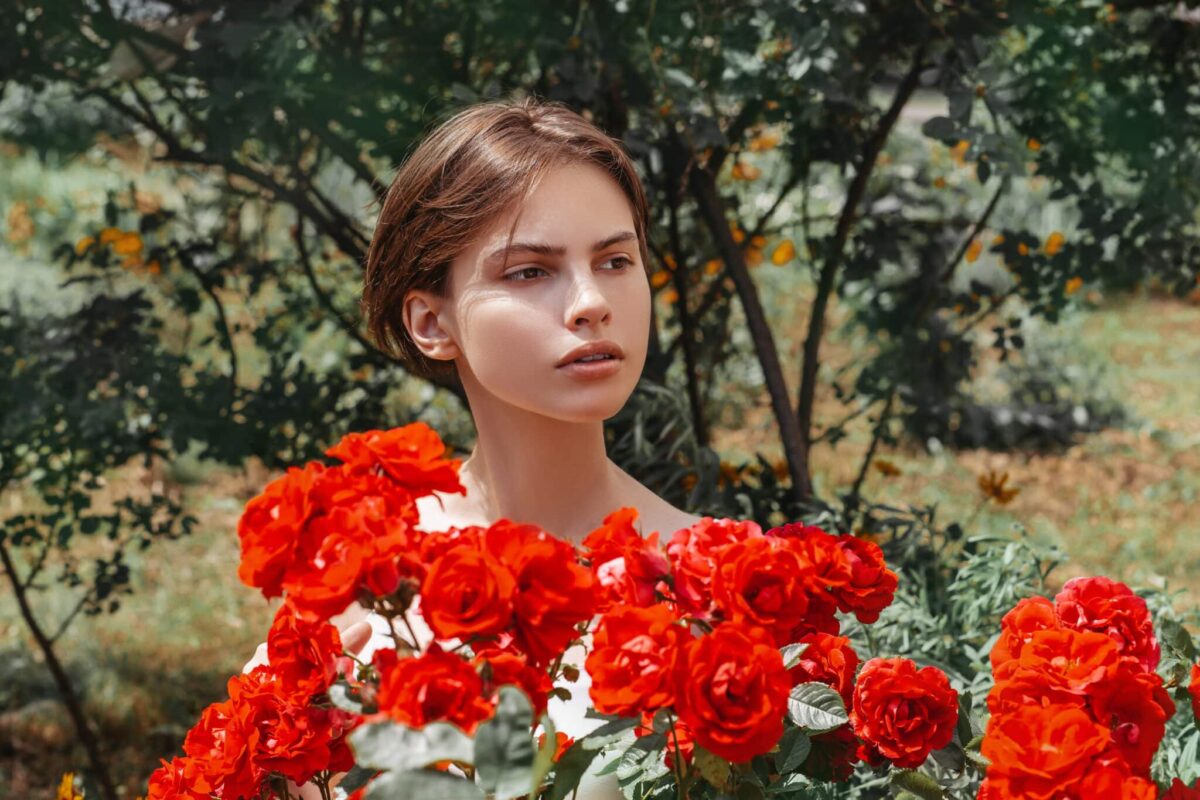 Beautiful girl behind a blooming red rose bush