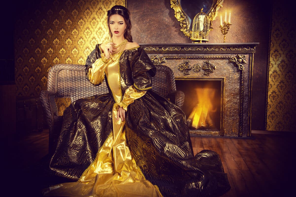 renaissance lady dressed in a golden gown, sitting by the fireplace