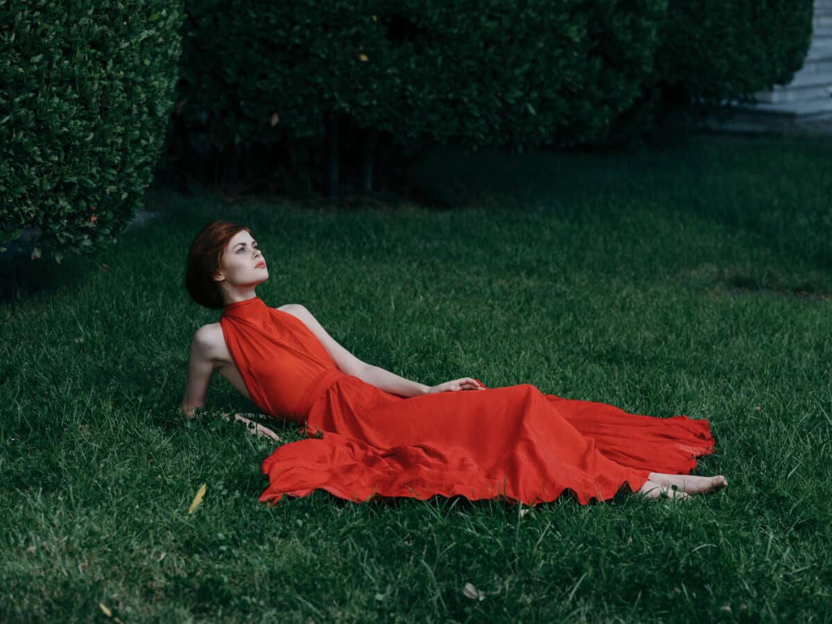 elegant woman in a red dress lies on the grass outdoor