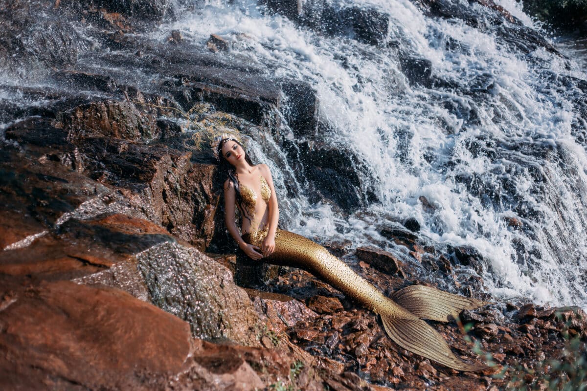 Art Fantasy woman real mermaid myth goddess of sea. gold fish tail creative costume ocean siren sexy body. spa relaxation. wet girl mystic spirit of river lies resting in waterfall. nature magic water