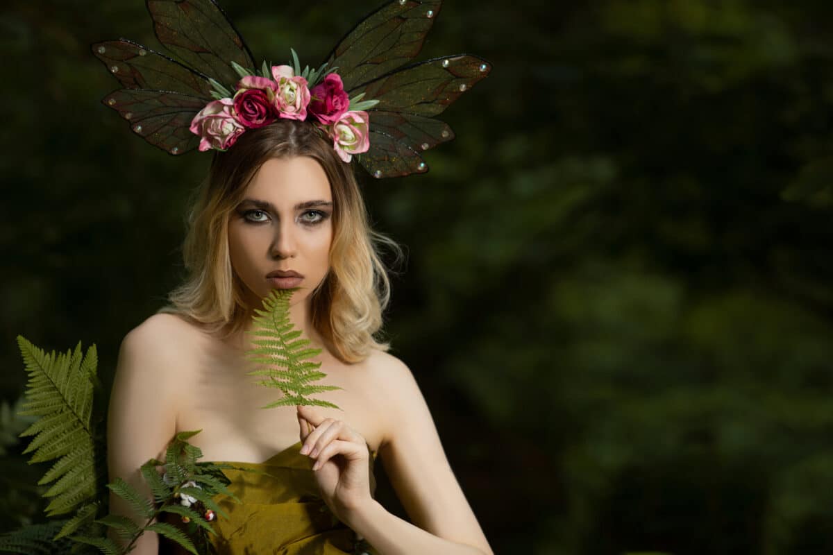 Portrait of Caucasian Female Posing With Decorative Butterfly Garland and Holding Green Leave Against Natural Background.
