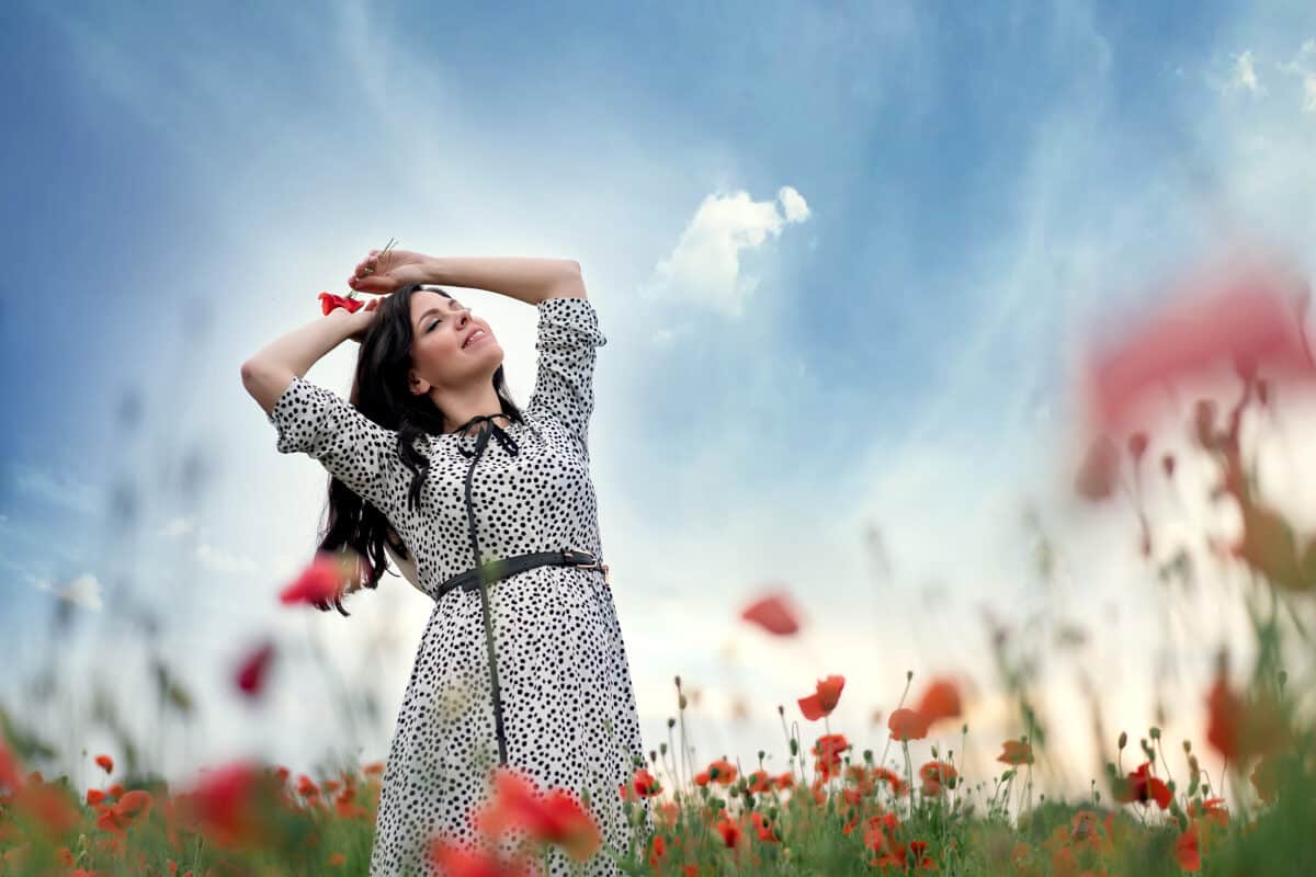 Beautiful lady standing in a field of poppy flowers with nice view of the sky