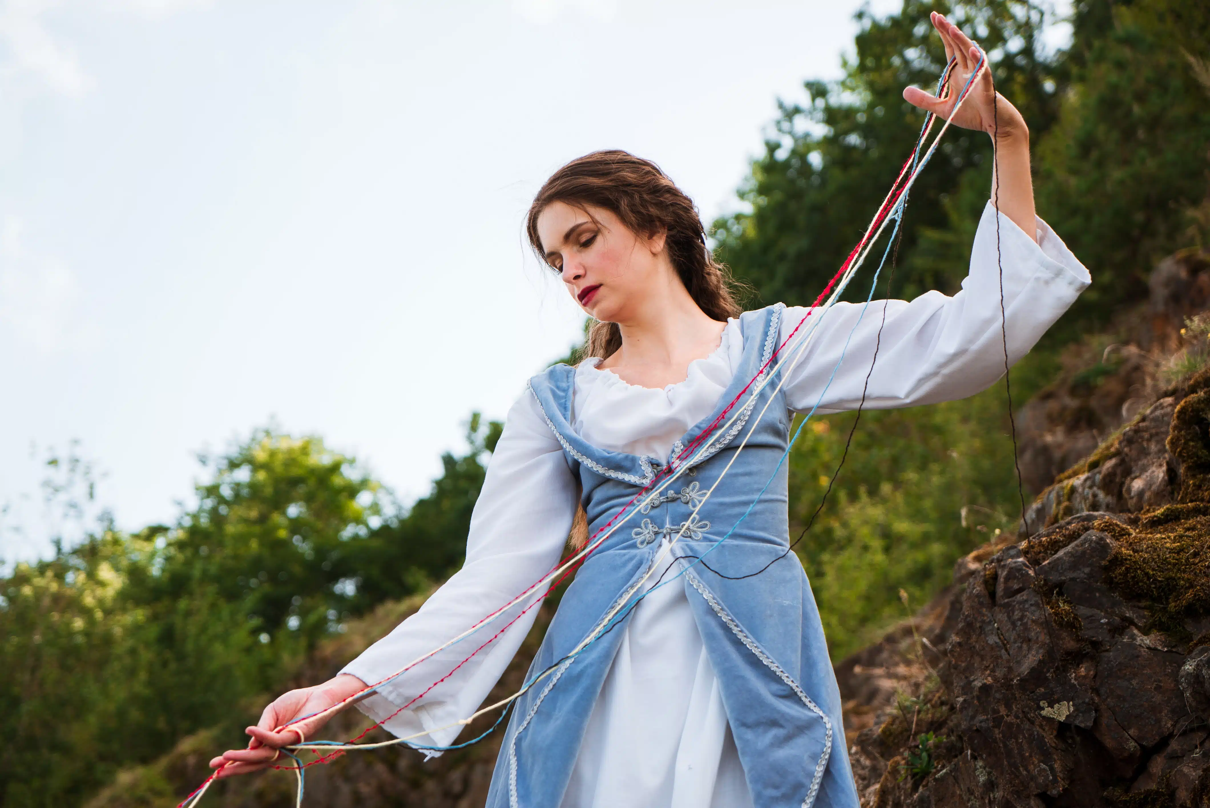 Vintage portrait of a beautiful noble lady in a white and blue dress near a rock with balls of thread 2.