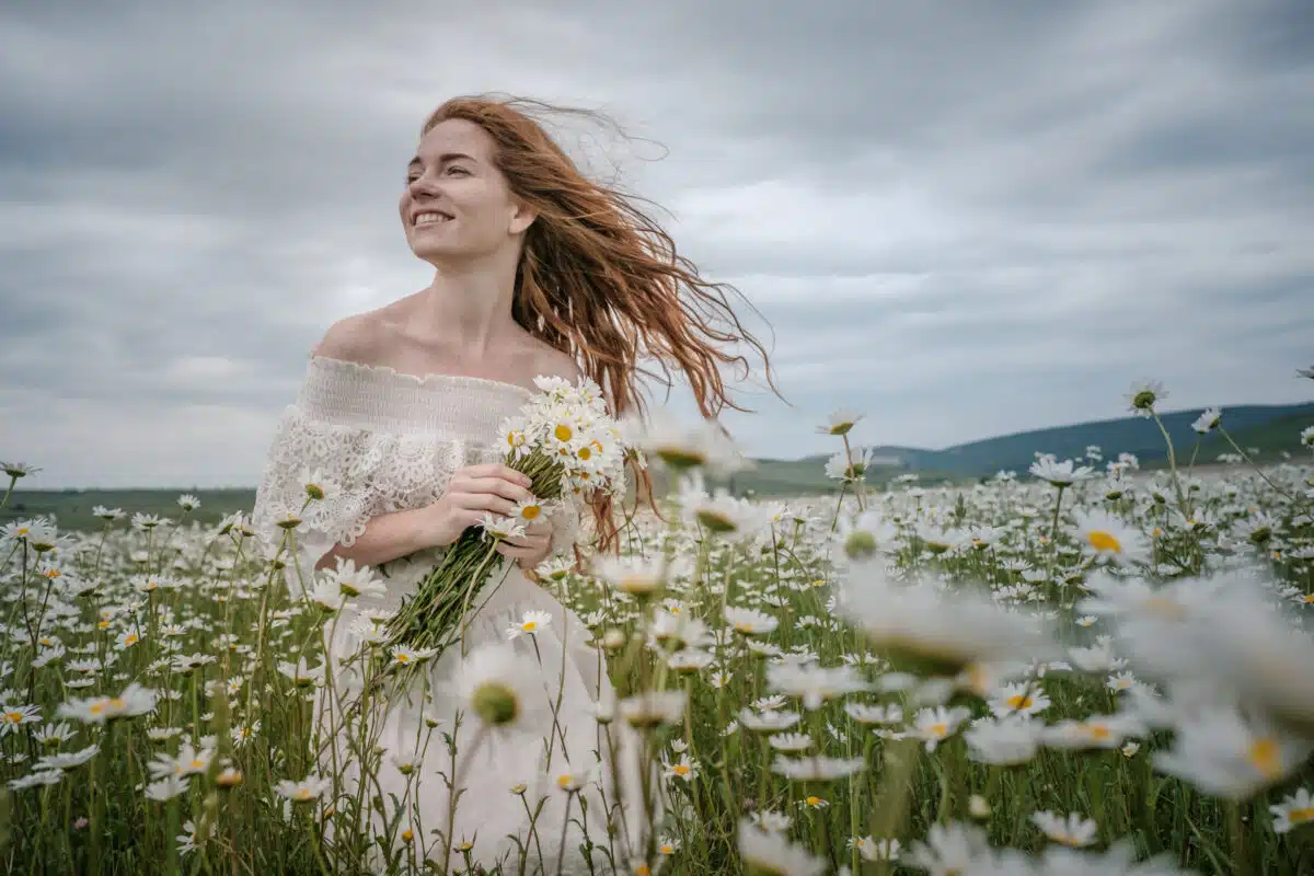 a beautiful young woman with curly red hair having fun in the chamomile field