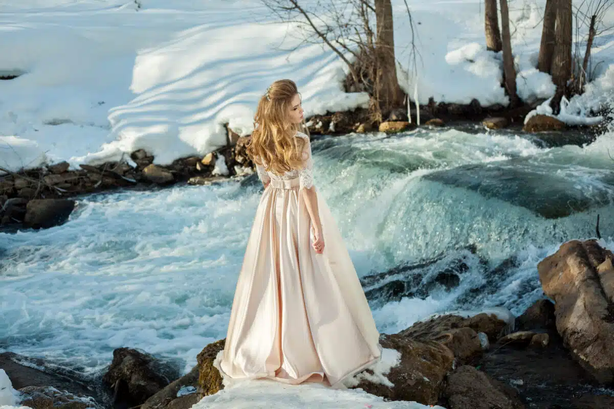 Beautiful young girl in a dress standing next to the frothy river