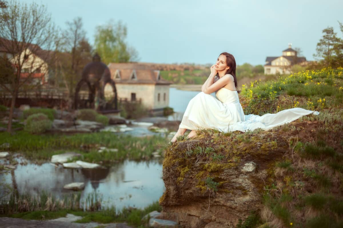 a beautiful young woman in a white dress sitting by the river