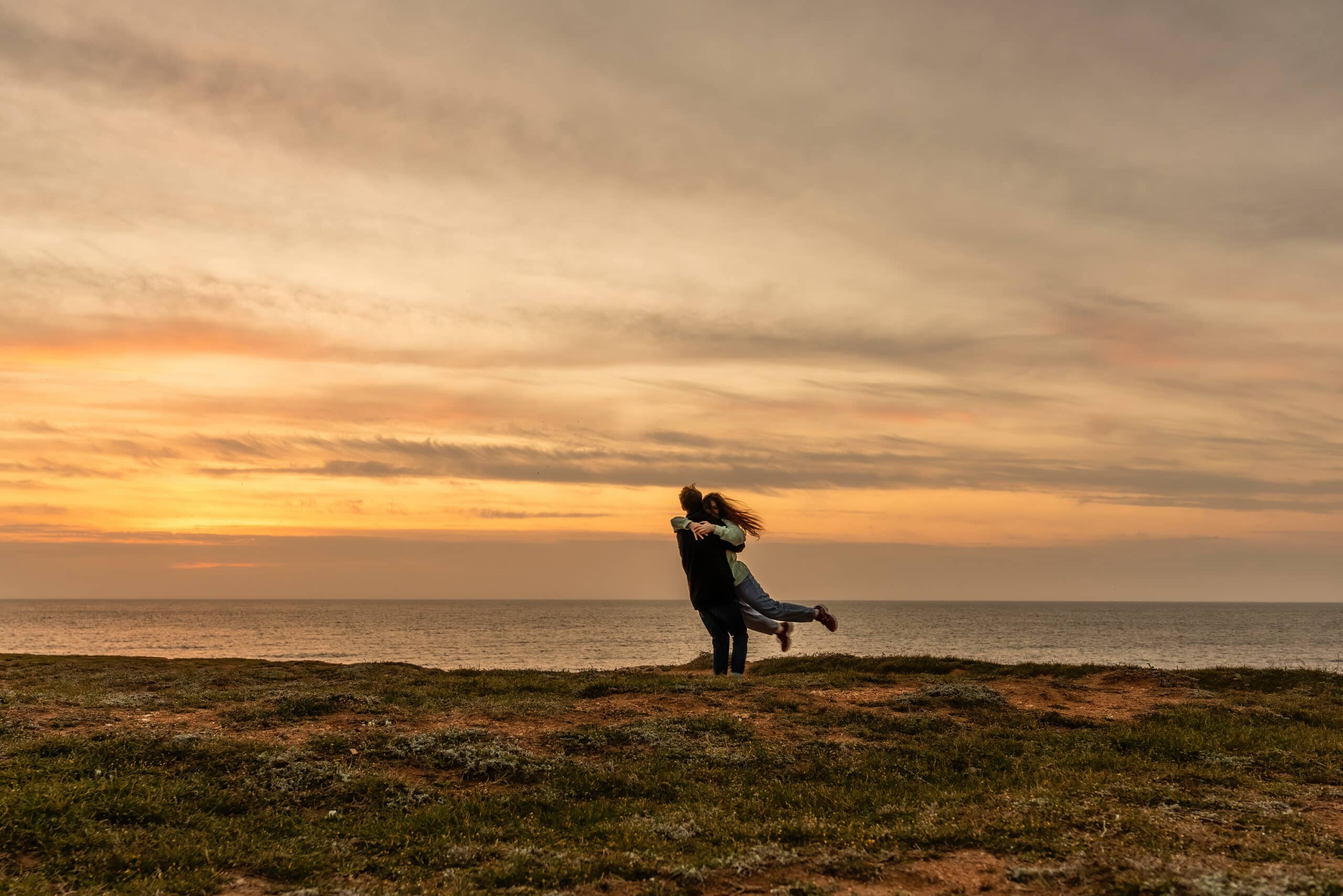 Portraits of lovers, romantic couple of lovers hugging, kissing, touching, eye contact at sunset, sunrise against the background of the sea, sun, clouds in fiery red, orange colors