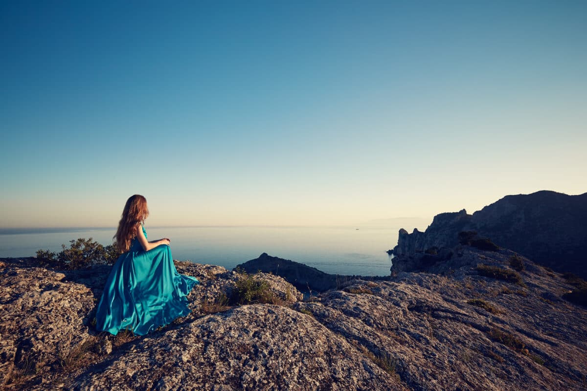 Young beautiful woman in a blue dress looking at mountains and sea