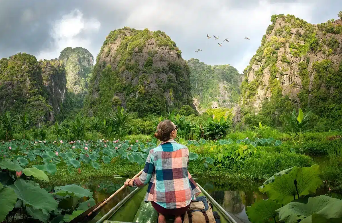 Woman traveling by boat on river amidst the scenic green karst mountains in vietnam.
