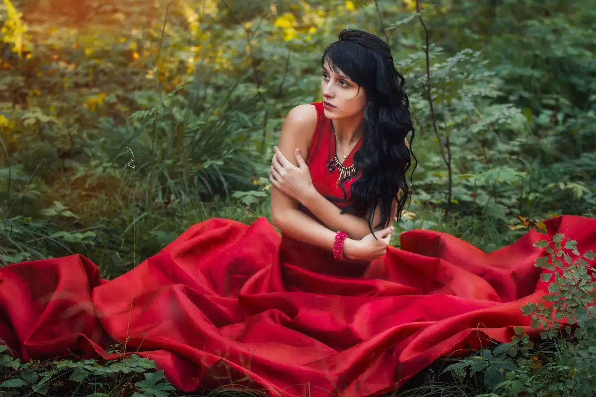 Mysterious woman in a long red dress sitting alone in the forest