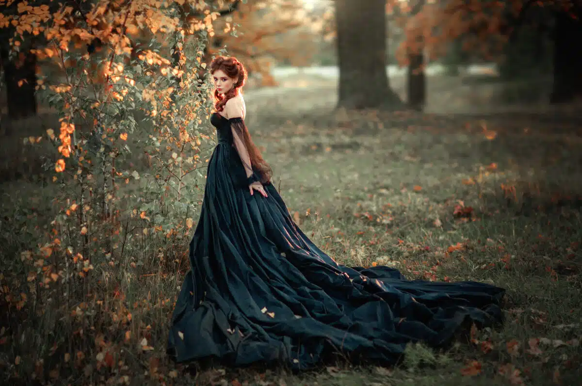 a magnificent red haired lady in a black dress in the woods