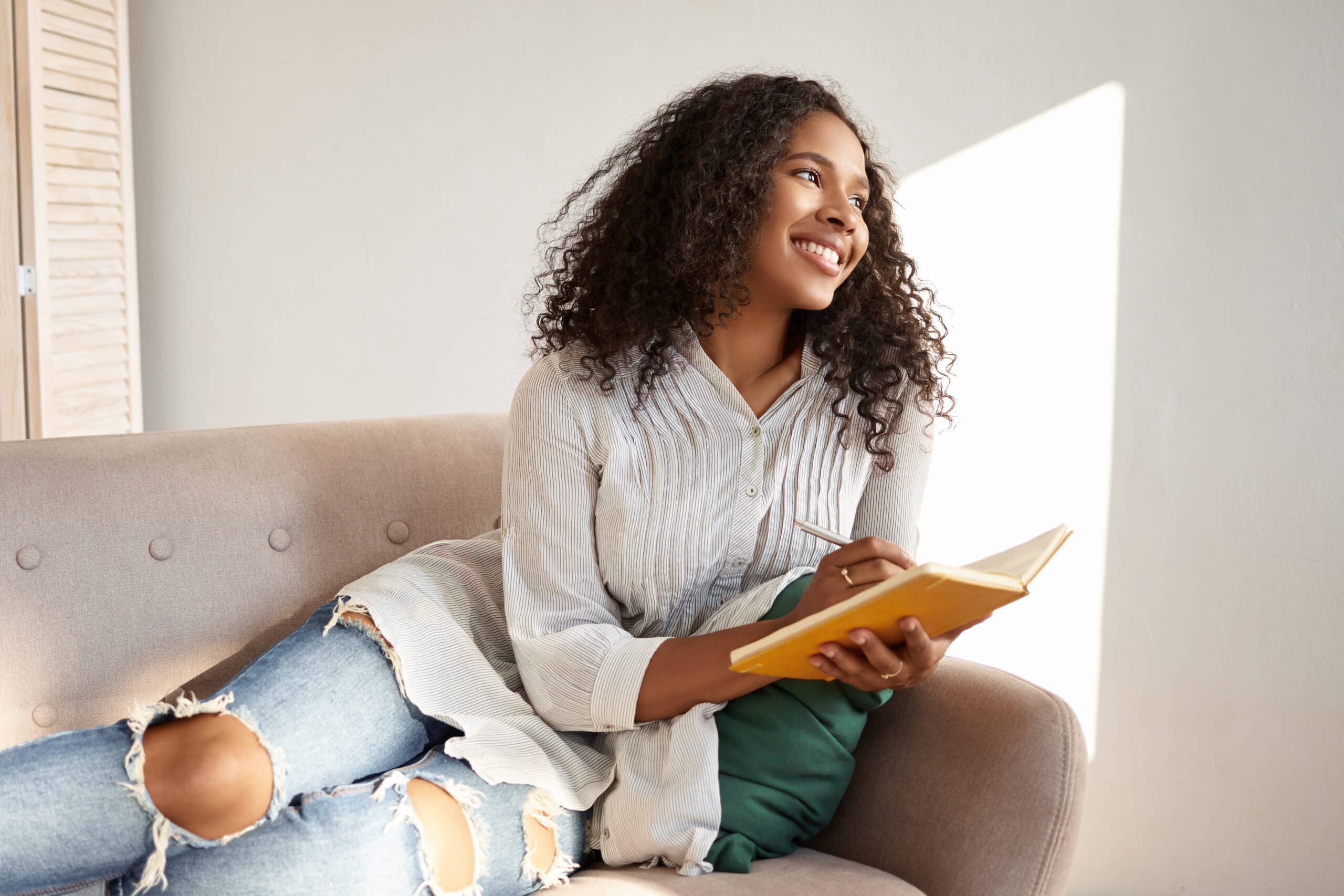 Cute Afro American young woman writing on the sofa.
