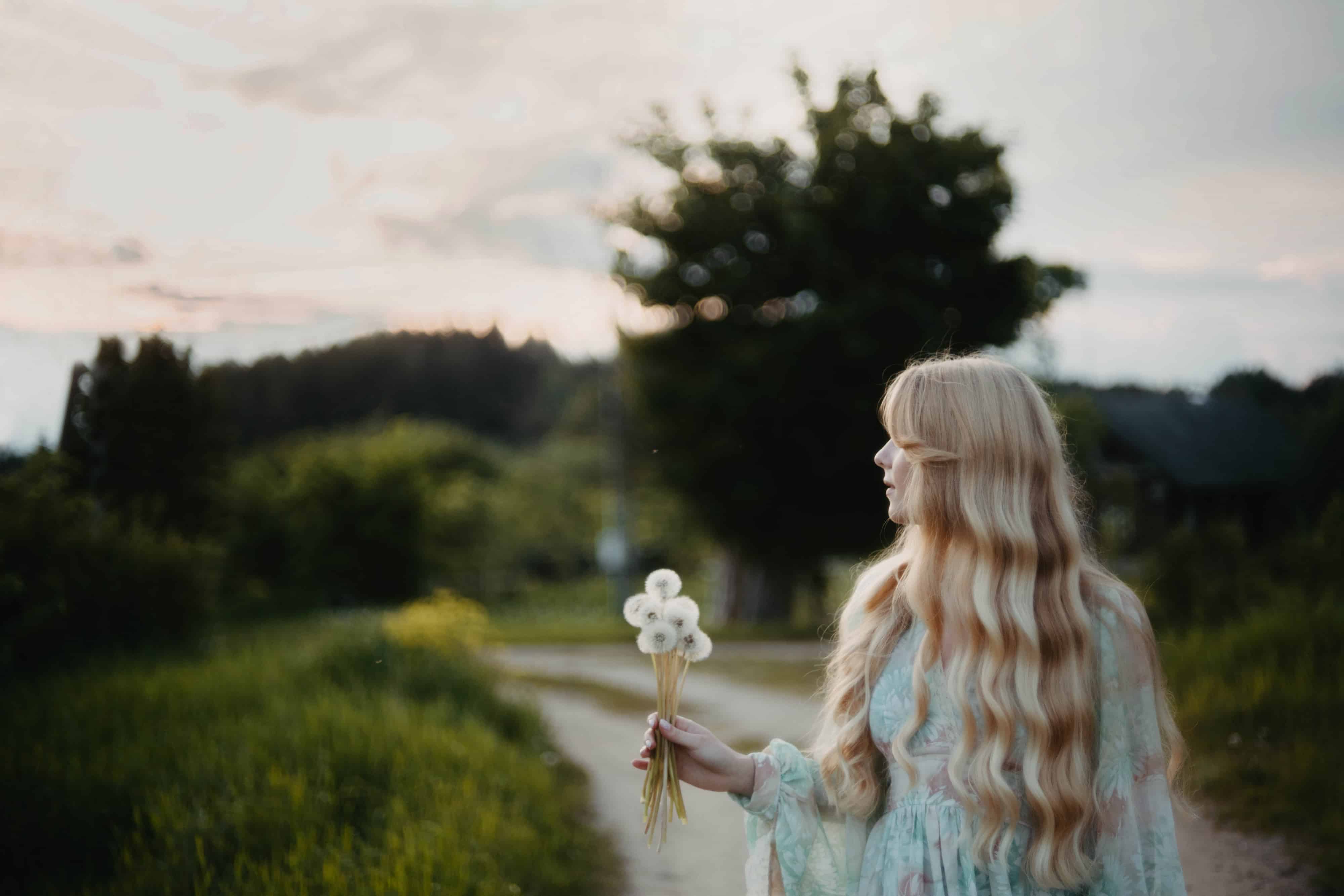 young long-haired blonde in a dress with dandelions in her hands