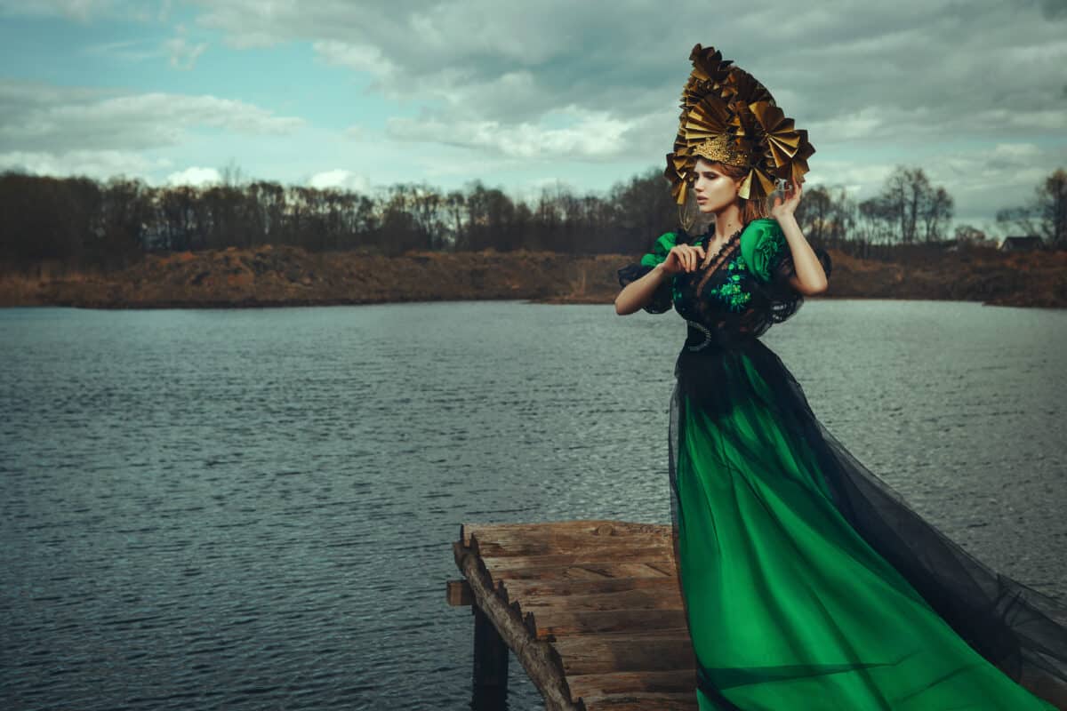beautiful princess dressed in green standing on wood dock by the lake
