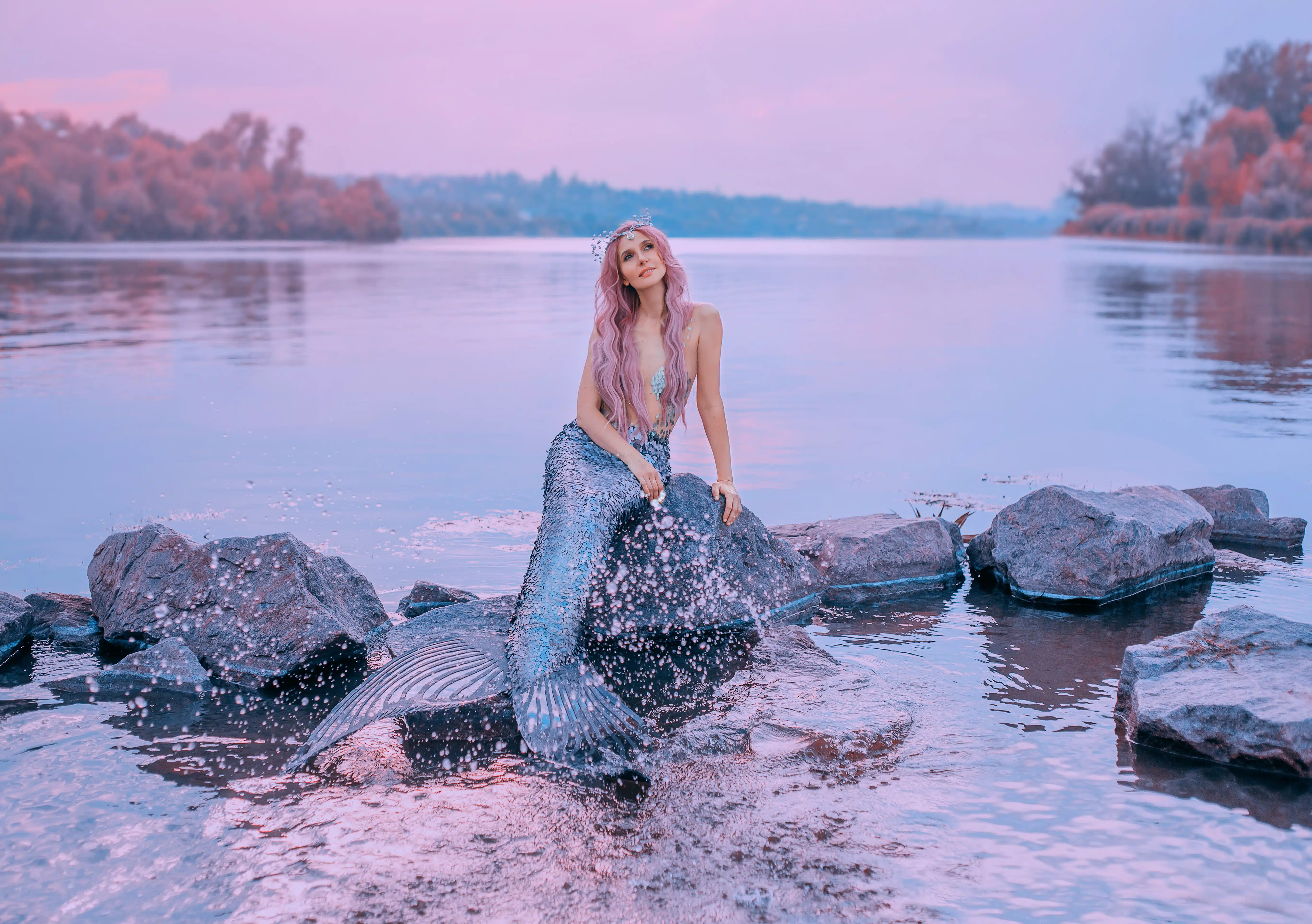 mermaid sea queen with pink long hair dreamily looks at purple sky with splashes of water around her tail