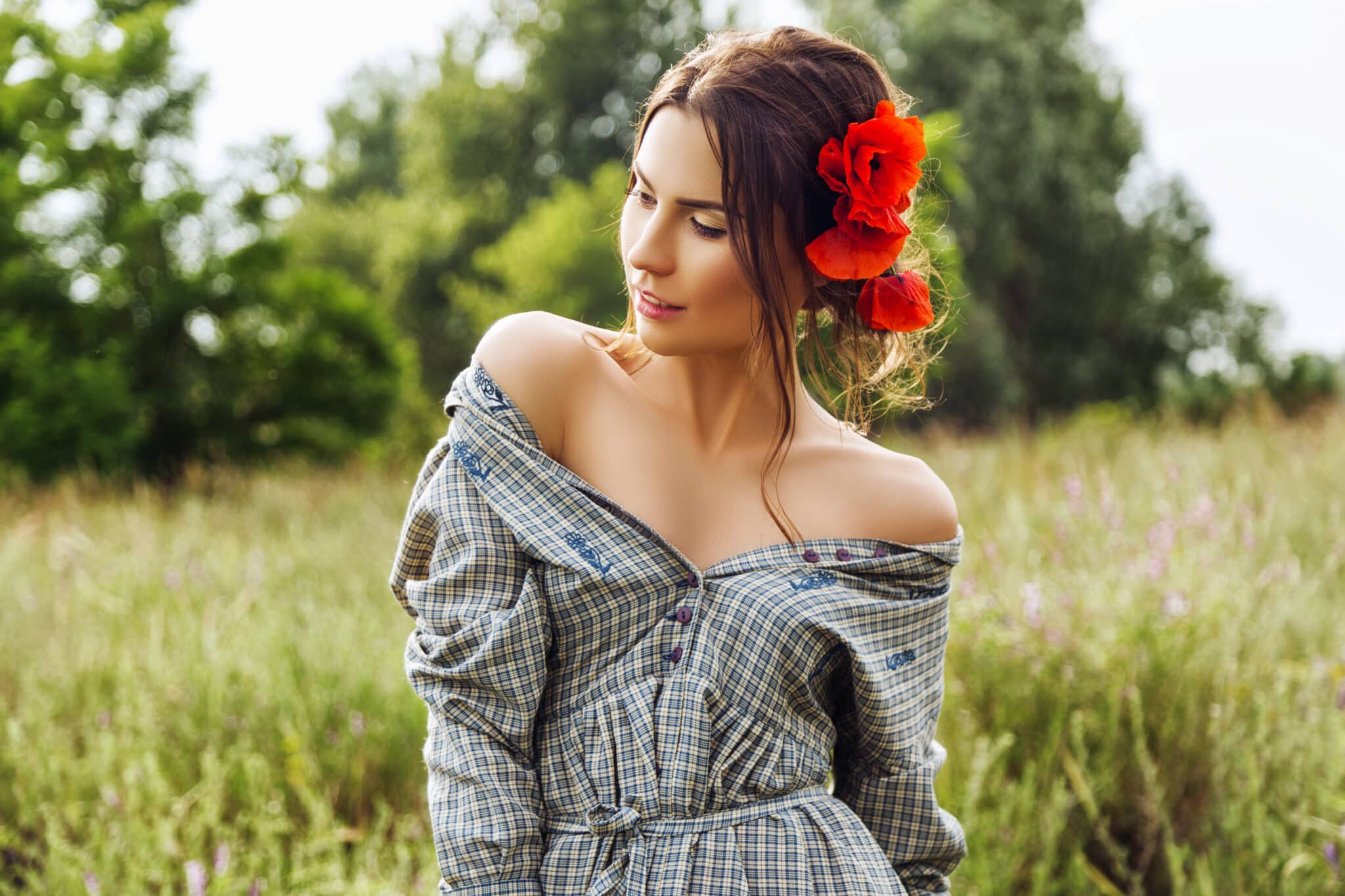 a beautiful brunette woman in dress with red flowers in her hair in the field