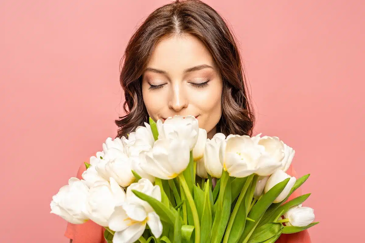 Happy woman with closed eyes smelling the bouquet of white flowers in her hands.