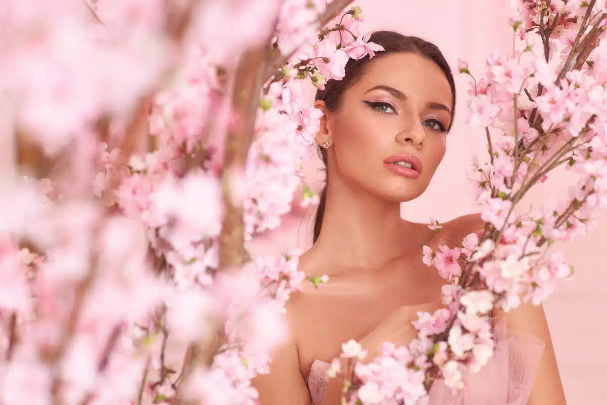 a lovely brunette woman looking through trees with pink blossoms