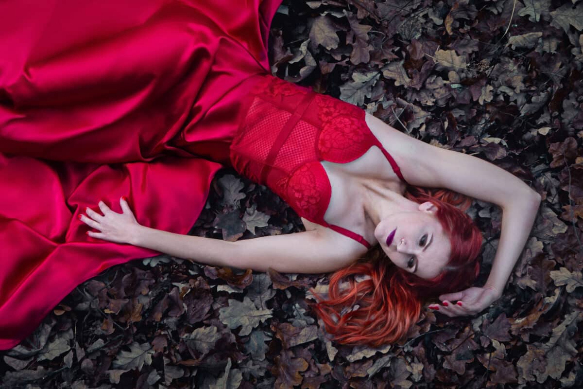 beautiful lady lying on the ground in red dress in a dark forest