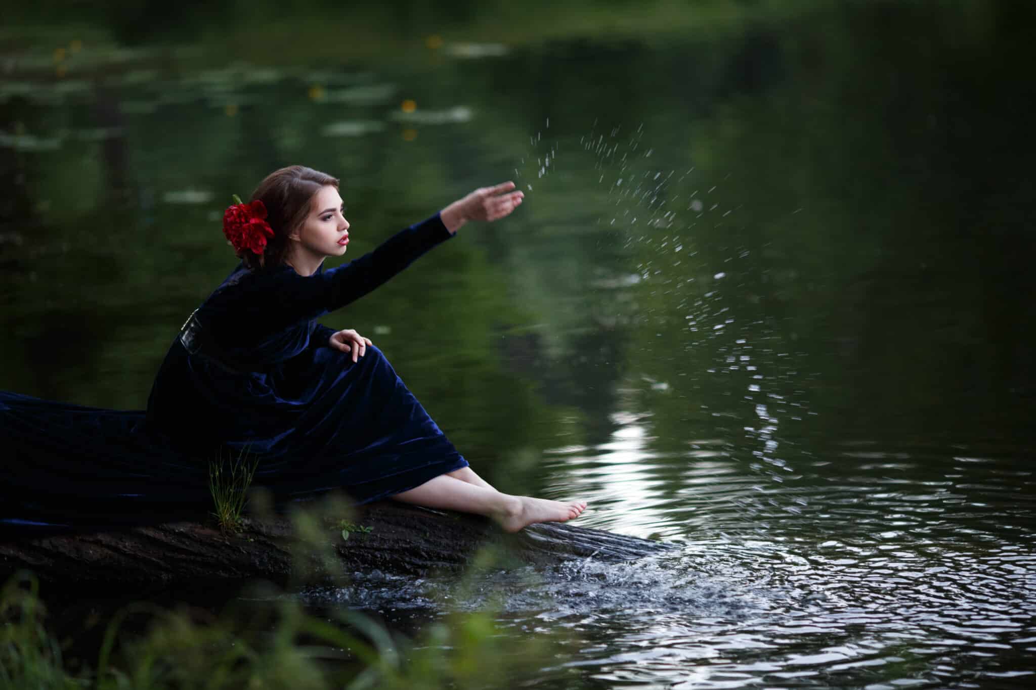 Beautiful lady in a long blue dress on the shore of a forest lake