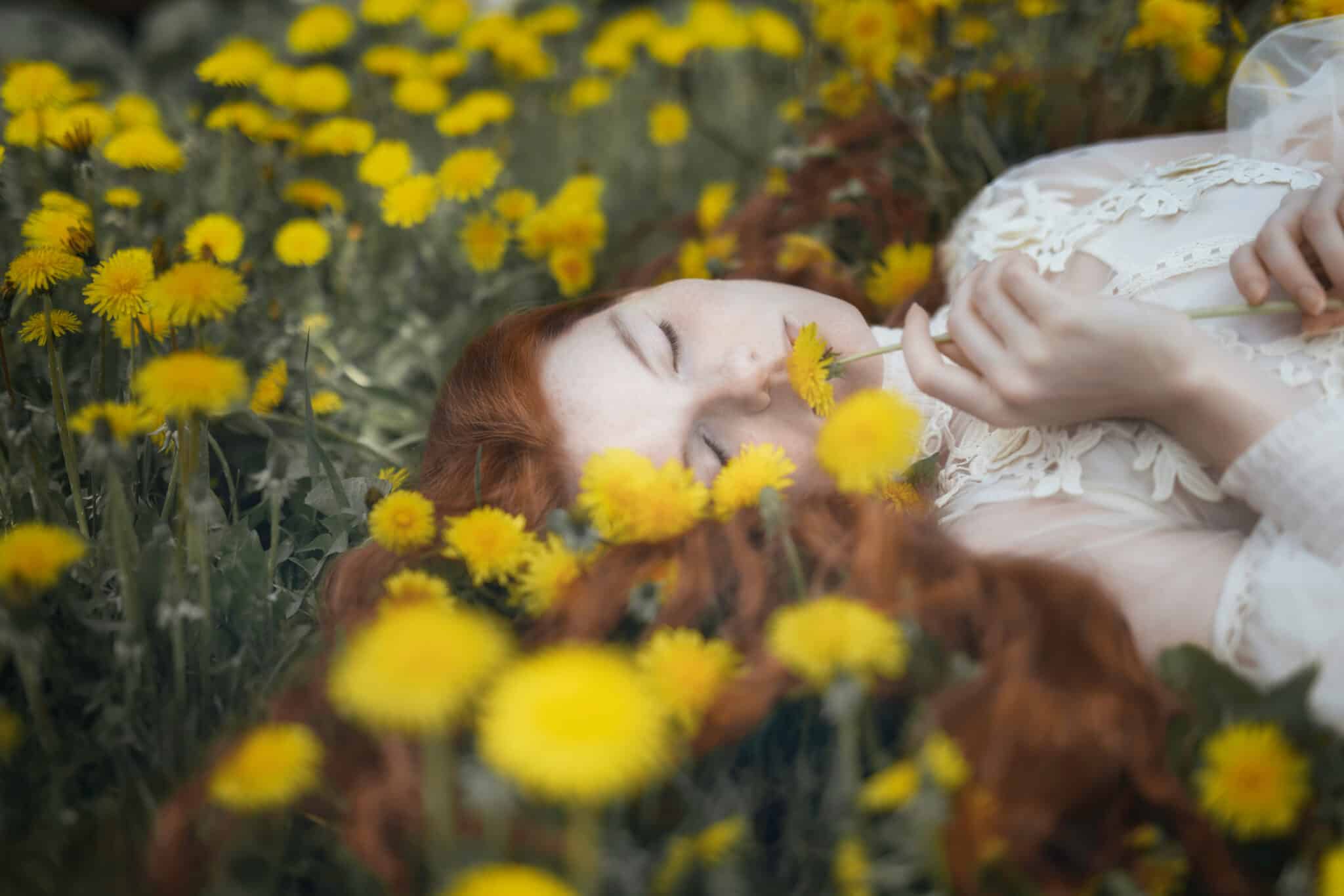 red-haired woman with closed eyes lying among yellow dandelions