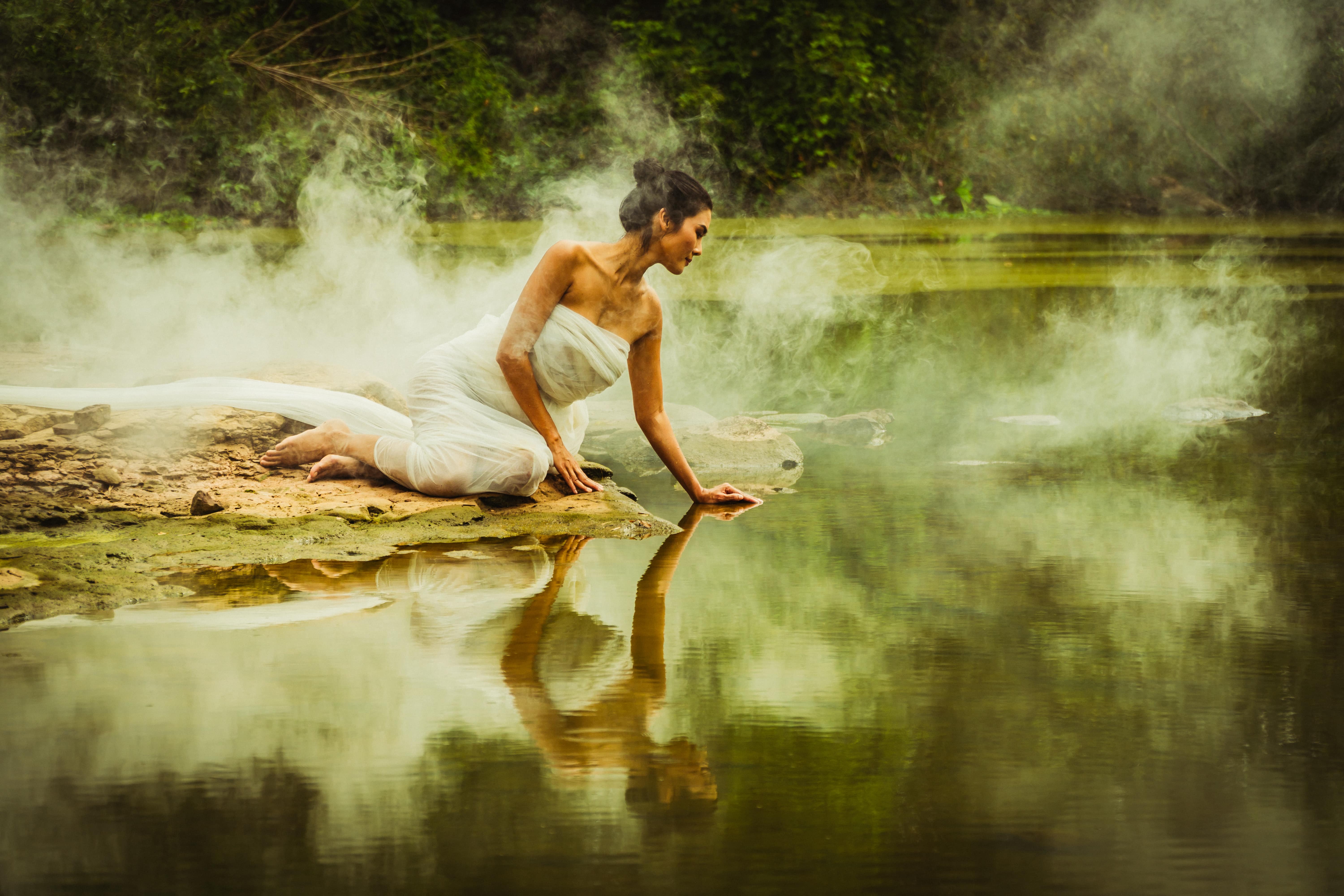 enchanting woman sitting on the ground by the misty river