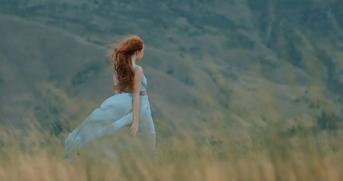 a red haired maiden walking down the trails on meadow with scenic mountain background