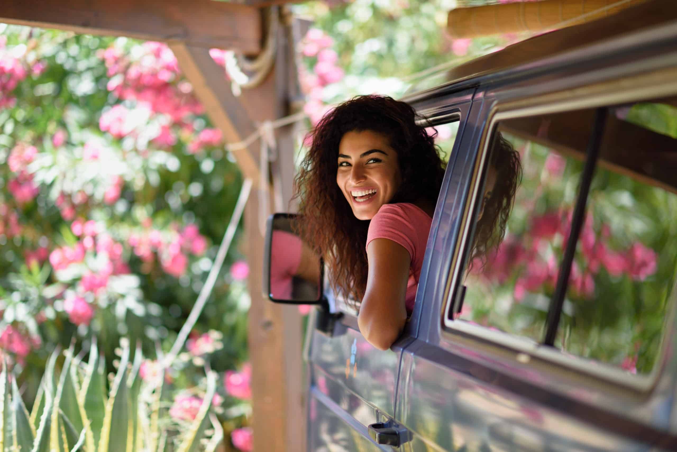 Young woman in a camper van in a beautiful camping with pink flowers.