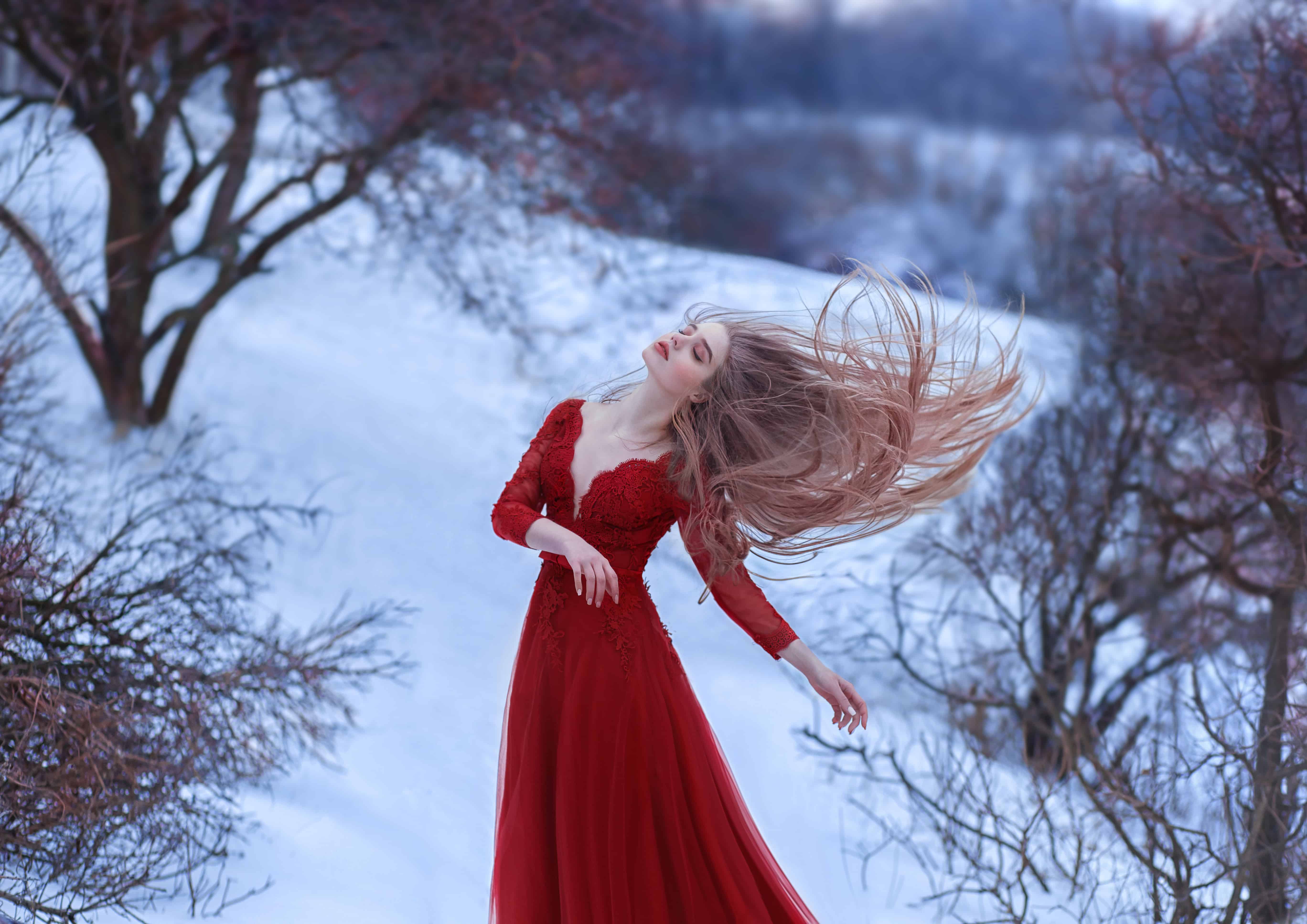 A young girl dances in the wind, her hair is beautifully fluttering. The pose is light and airy, a sense of freedom. Lady in a red dress on a background of a picturesque winter. Artistic photography.