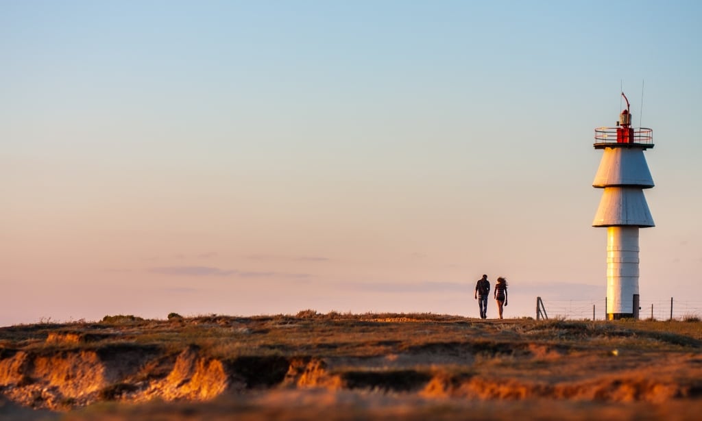 A loving guy and a girl are walking at sunset along the coast, near the lighthouse.
