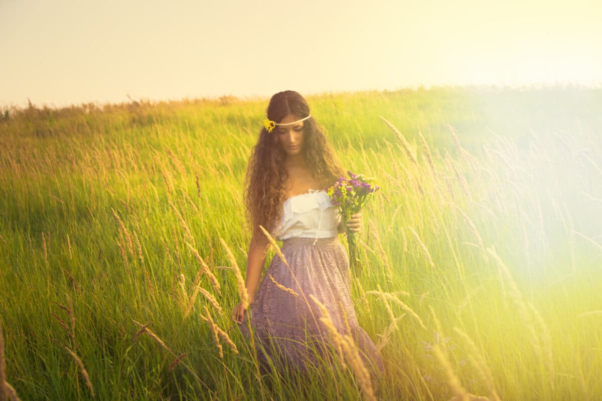 an enchanting lady with long curly hair holds in hand a bouquet of wild flowers in light at grass field