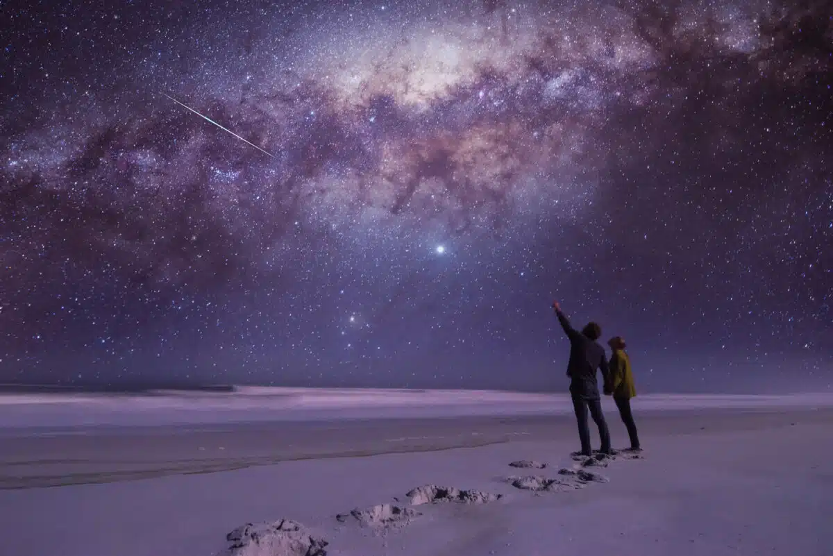 Couple holding hands pointing in amazement at a shooting star in the vast star-filled sky
