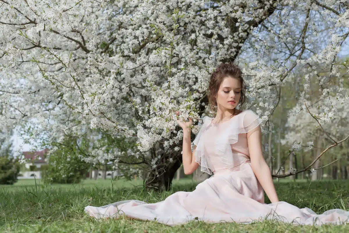 beautiful tender sweet girl in a pink dress with a hairdo near blossoming tree on a sunny spring day