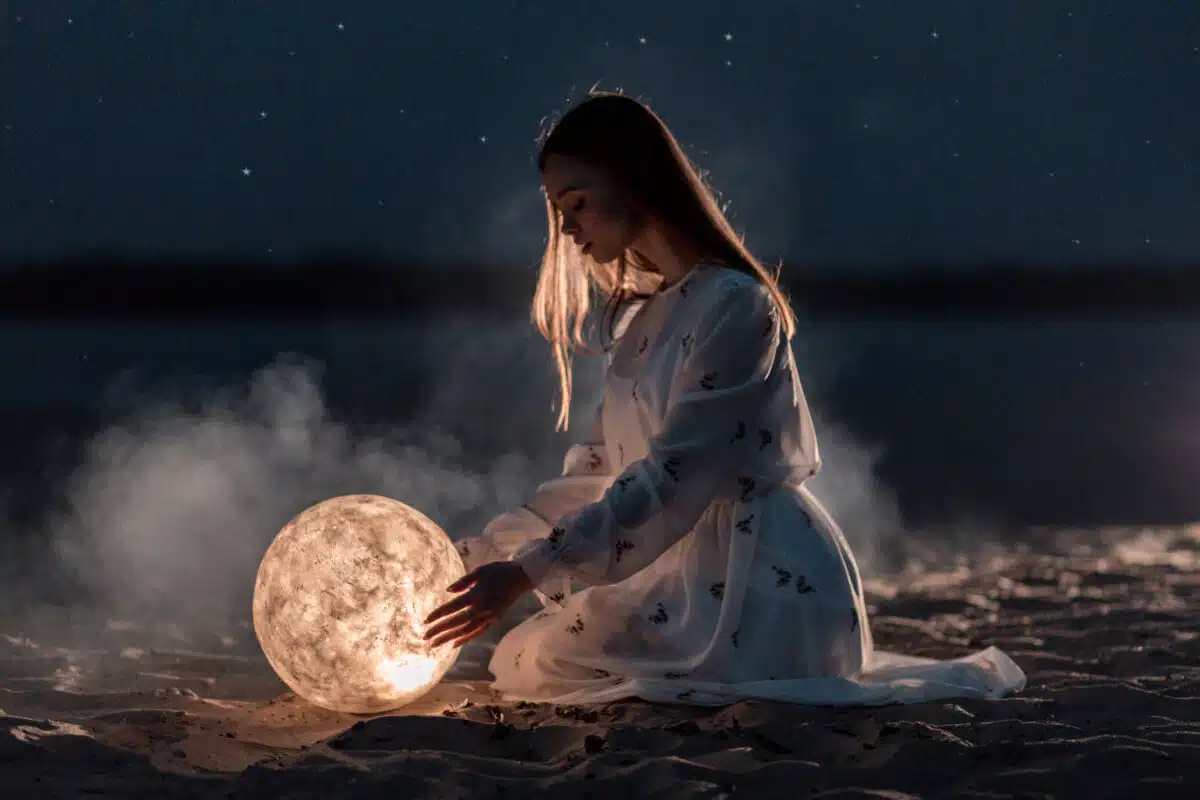 Beautiful young girl on a night beach with sand and stars holds the moon in her hands