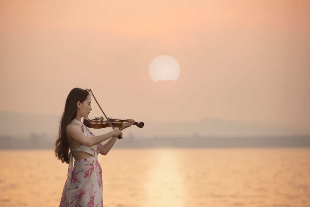 Beautiful woman playing violin at the sea with sunrise background